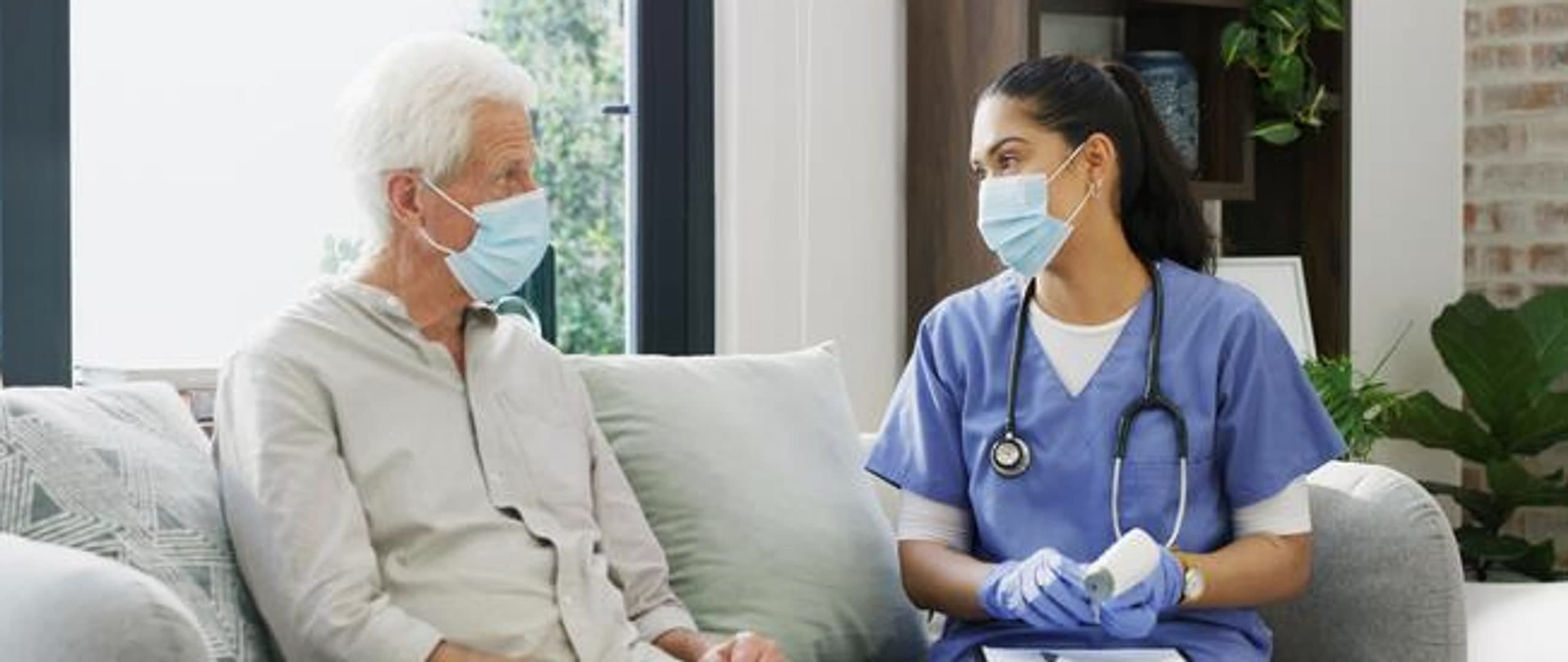 Home health nurse consulting with an elderly man on a couch