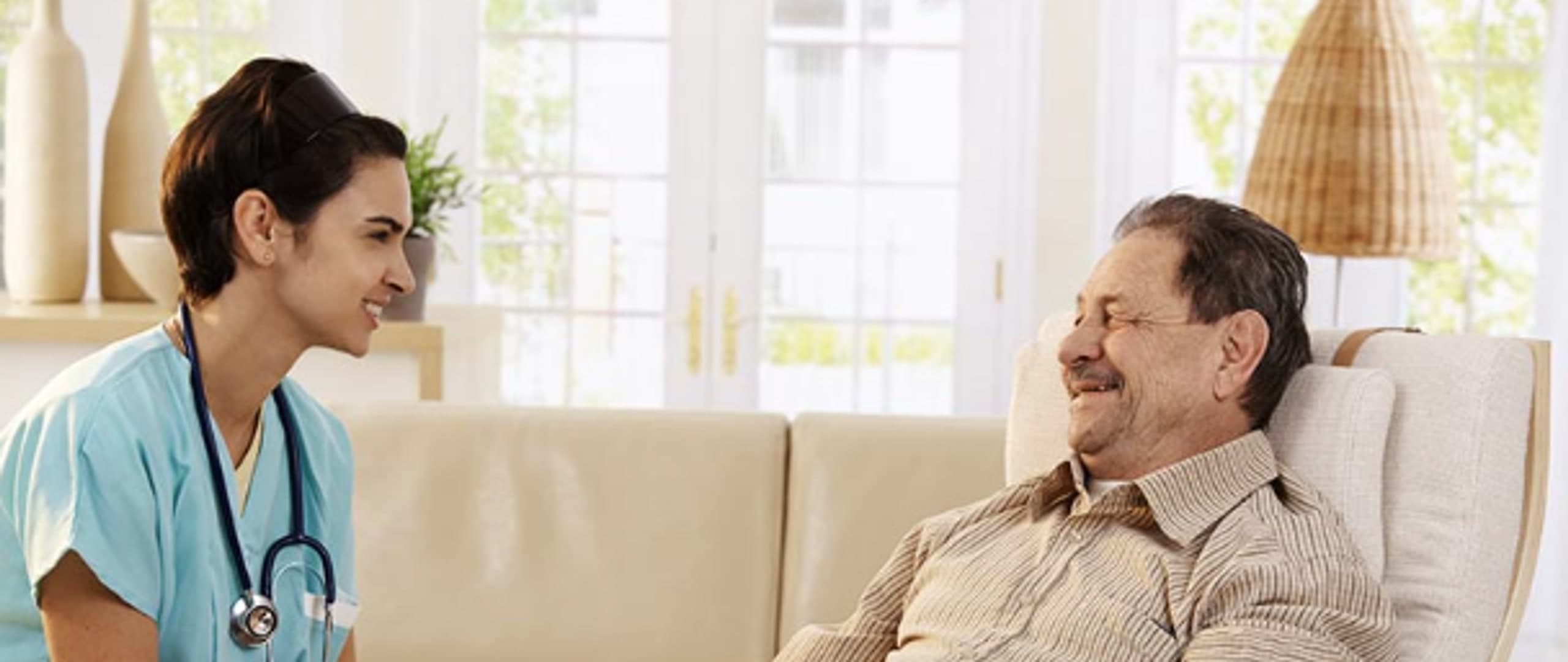 Nurse holding the hand of a smiling elderly man in a recliner