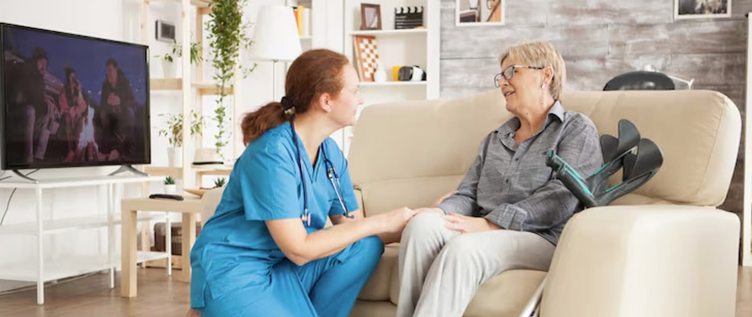 Nurse kneeling beside a smiling elderly woman during a home visit