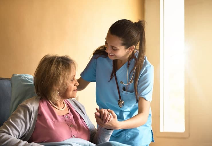 A home health nurse holding the hand of a smiling elderly client